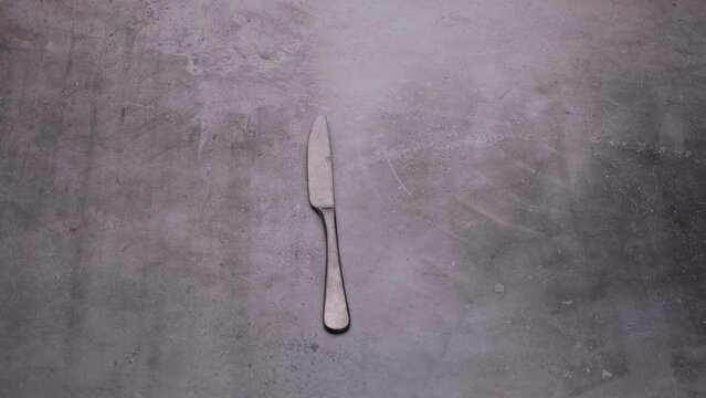 Frosted vintage knife is spinning on the table, a video of cutlery on a gray background.