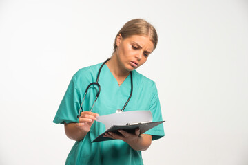 Blonde female doctor in blue uniform checking the history of the patient and looks confused