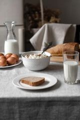 the table is covered with a linen tablecloth and on it are natural and healthy products, milk and cottage cheese, bread and boiled chicken eggs