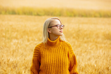 Stylish girl in eyeglasses and yellow sweater in wheat field