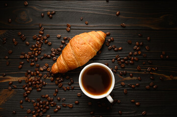 Croissants with coffee and coffee beans on a wooden background.