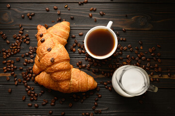 Croissants with coffee and coffee beans on a wooden background.