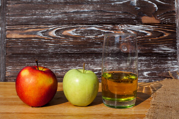 A glass of freshly squeezed apple juice and a red and green ripe apple on a table covered with a...