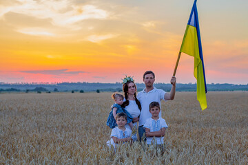 Happy smiling family in national Ukrainian embroidered shirts hold large yellow-blue flag against background of spikelets of wheat field. Patriotic education. Independence Day. Glory to Ukraine