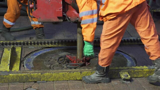 Drilling platform. Rotor table. Manual slips is being installed. Drill pipe is lowered. Legs in orange coveralls. Drill floor. RIG.