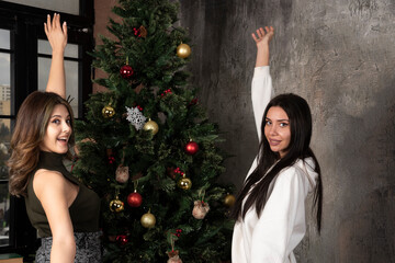 Two happy young women standing near Christmas tree in living room