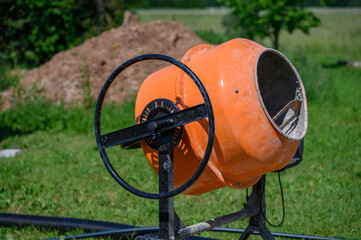 Concrete Mixers. Small. Orange. For home repairs. For doing simple jobs. Concrete is made with an electric concrete mixer, the photo was taken outdoors on a sunny summer day.