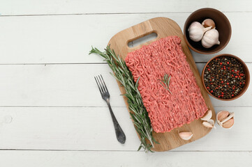 Fototapeta na wymiar Fresh raw meat or ground chicken meat on a wooden cutting board with thyme, spices and garlic. White wooden background. Top view. Copy space.