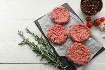 Raw beef burger patties on butcher's wooden board, rosemary and pepper. White background. View from above.