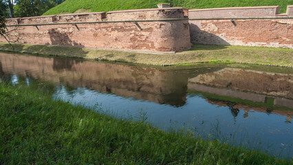 Fortress moat with water reflecting trees and castle walls. Bridge over the moat.