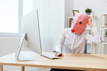 Thoughtful crazy businesswoman worker freelancer in pink fish mask work on computer online...