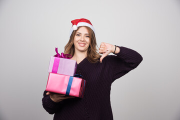 Young woman in Santa hat with gift boxes showing a thumb down