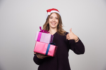 Young woman in Santa hat with gift boxes showing a thumb up