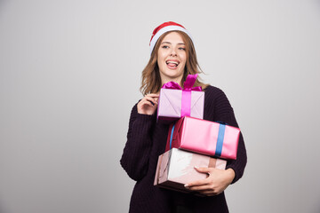 Fototapeta premium Young woman with Santa hat carrying gift boxes presents