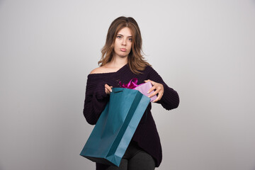 Photo of young woman pulling gift from shopping bag