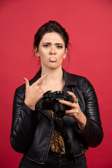 Cool girl in black leather jacket holding her professional camera and looks dissatisfied about her photo history