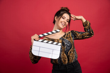 Brunette girl holding a blank clapper board for film production on red background