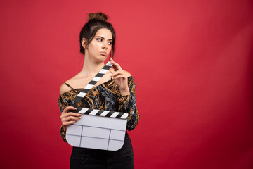 Brunette girl holding a blank clapper board for film production on red background