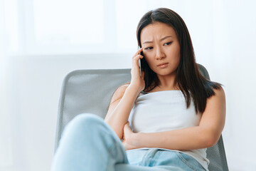 Confused upset tanned lovely young Asian woman listen shocked news at call using phone at home interior living room. Distance communication Social media concept. Cool offer Banner Wide angle