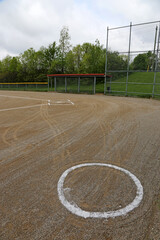 The on deck circle of an unoccupied baseball field on a cloudy day.