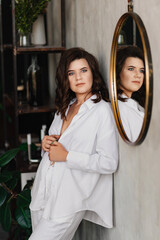 a brunette woman in a white shirt near the round mirror. cozy home clothes. 