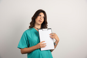 Tired doctor posing with clipboard on white background