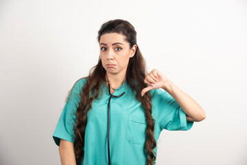 Portrait of female healthcare worker posing with thumb down on white background