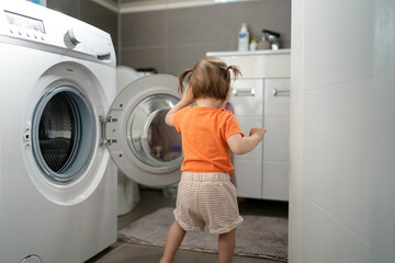 One girl small caucasian toddler child daughter standing at the washing machine in the toilet opening or closing the door examine and learn early development and growing up mischief concept copy space