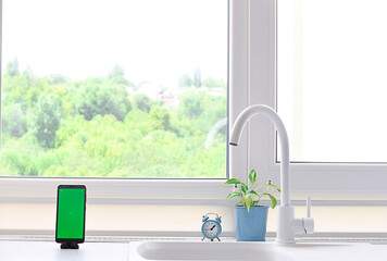 Smartphone with a green blank screen on the kitchen table against the background of the window.