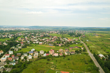 Fototapeta premium Aerial landscape view of village houses and distant green cultivated agricultural fields with growing crops on bright summer day