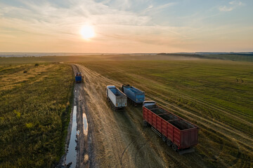 Aerial view of cargo truck driving on dirt road between agricultural wheat fields making lot of...