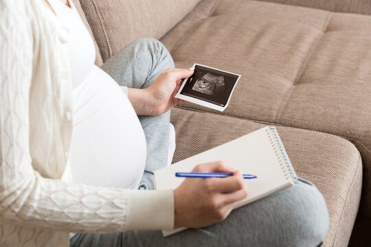 Top view caring future mother writing diary with ultrasound. pregnant woman tummy making notes feeling during pregnancy or creating scrapbook