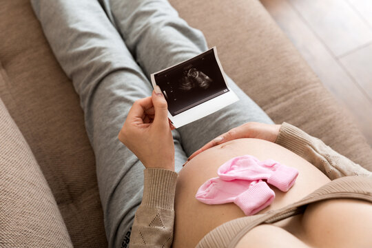 Pregnant Woman sitting on bed and Looking At Ultrasound Scan photo of her Baby. A pregnant female shows her ultrasound report and her unborn baby