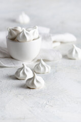 White meringue cookies in a white bowl with a white napkin, on grey background. 