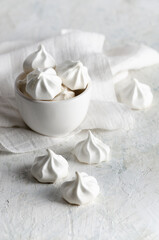 White meringue cookies in a white bowl with a white napkin, on grey background. 