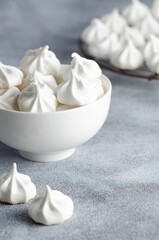 Fototapeta na wymiar White meringue cookies in a white bowl with a white napkin, on grey background. 