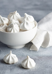 Obraz na płótnie Canvas White meringue cookies in a white bowl with a white napkin, on grey background. 