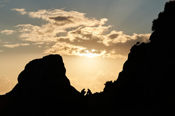 Isolated silhouette of two mountaineers in the distance in the background in high mountain at sunset. Hiking with unrecognizable couple. Concept of adventure, lifestyle, sport, nature, bravery...