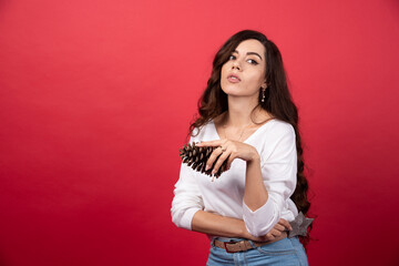 Young woman holding a big Christmas pinecone on red background