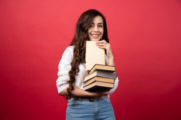 Young woman carrying books and smiling on a red background