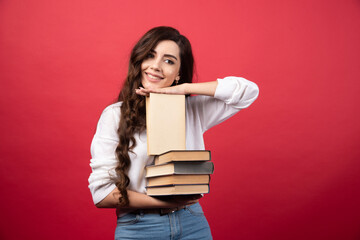 Young woman carrying books and smiling on a red background