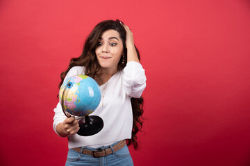 Brunette woman looking globe on red background