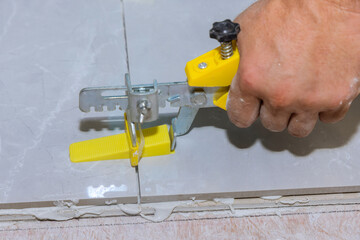 Working on tile leveling with plastic clips and wedges in a bathroom in process adhesive applying...