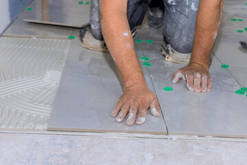 The placement of ceramic floor tiles on an adhesive surface with home bathroom construction workers