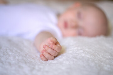 small hand of a sleeping baby on a white blanket. selective focus