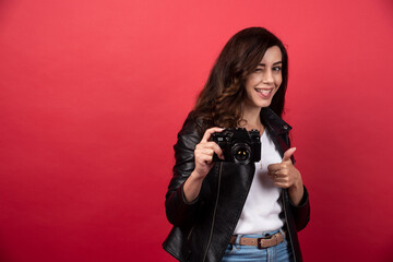 Woman photographer with a photo camera showing a thumb up on a red background
