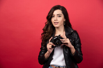 Beautiful woman photographer holding photo camera on a red background