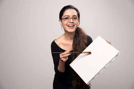 Young artist girl showing her artwork to the public and explaining details with the halp of brush