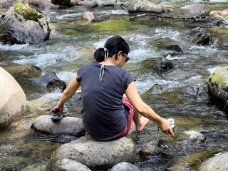 Woman resting on a large river rock while soaking her feet in the river