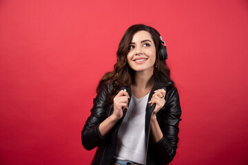 Young woman listening music in headphones and posing on a red background